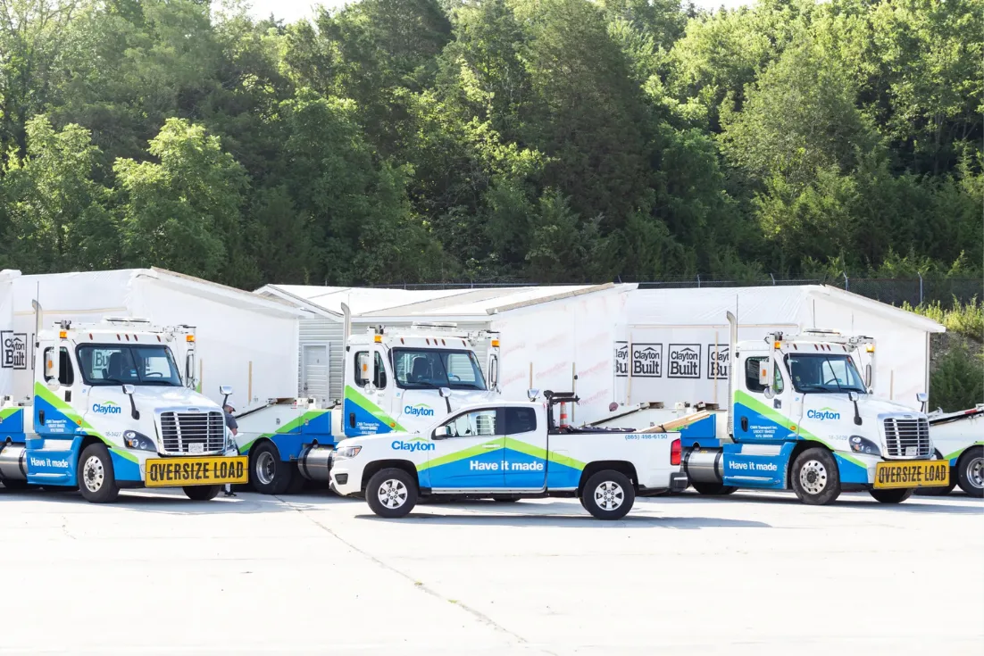 Three Clayton Connect home transport trucks attached to homes to be delivered are parked behind a Clayton branded pickup truck.