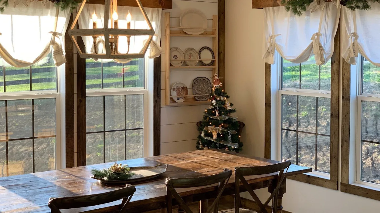 Dining room with wooden table, wooden chairs, large windows and farmhouse decor.