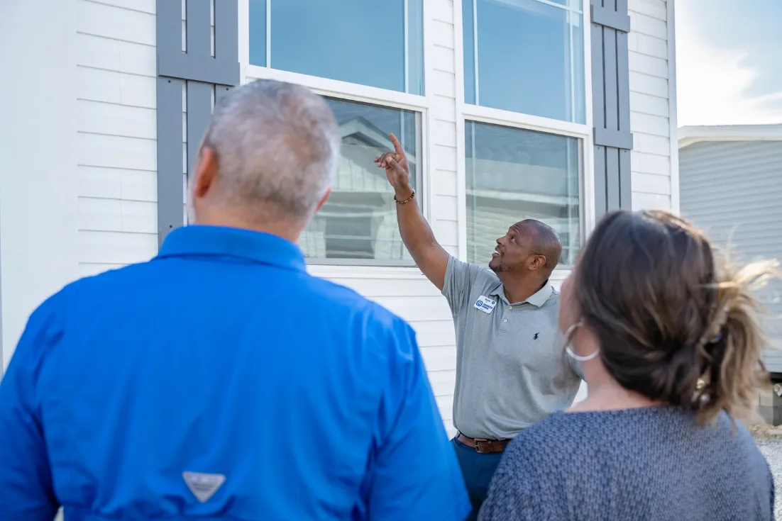 A home consultant in a gray polo points out exterior features of a home to couple at a Clayton location.