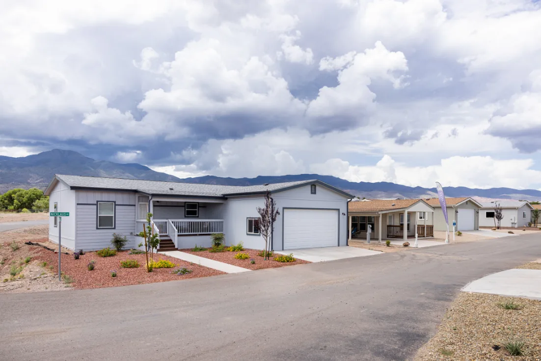 A row of blue and tan manufactured homes with attached garages on a neighborhood street.