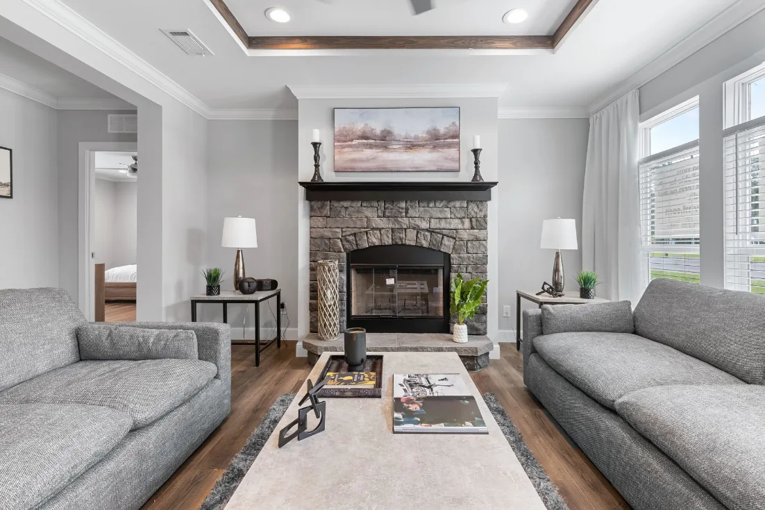 A living room with parallel gray couches, a stone fireplace, and a tray ceiling.