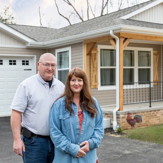 Couple stands outside of their CrossMod new construction home with attached garage and rooster sentry.