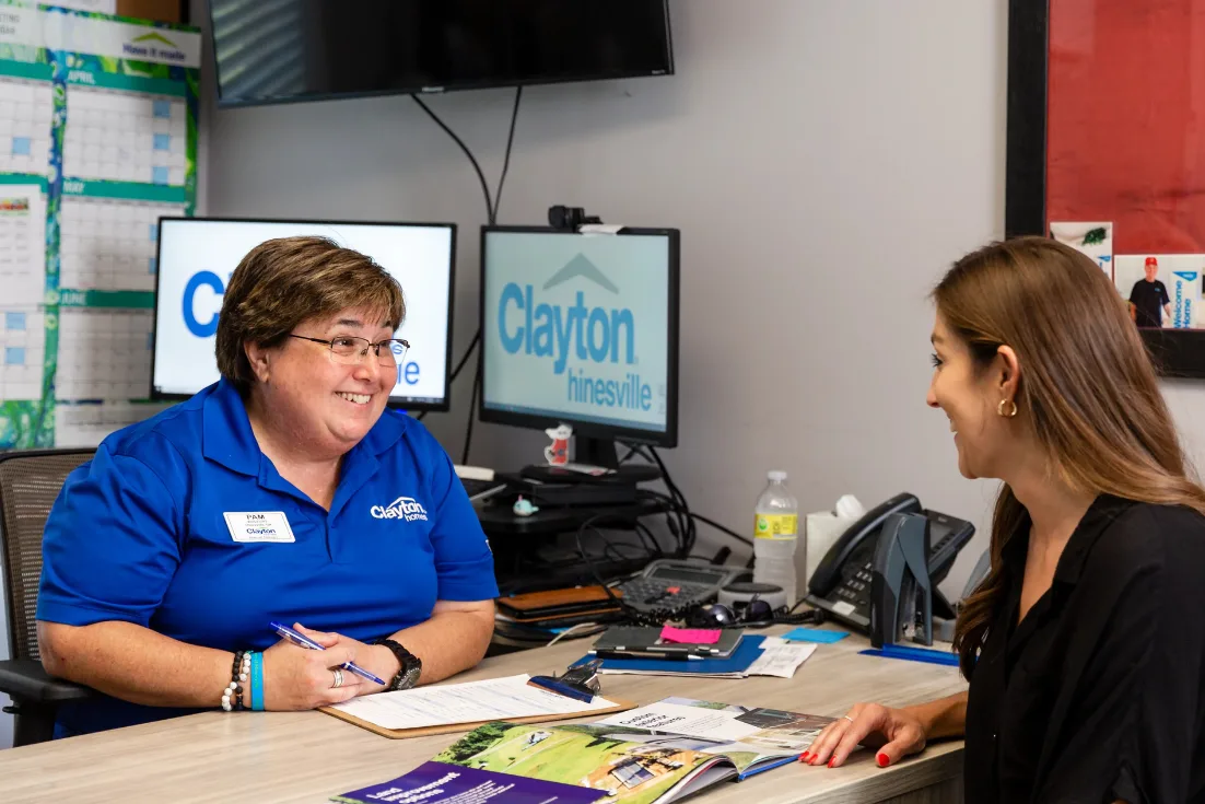 A home consultant in a blue polo talks with a woman at a desk.