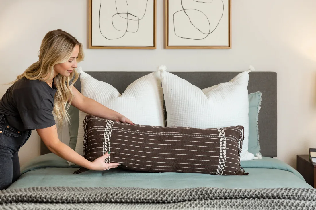Woman makes her bed in the primary suite of her new construction home.