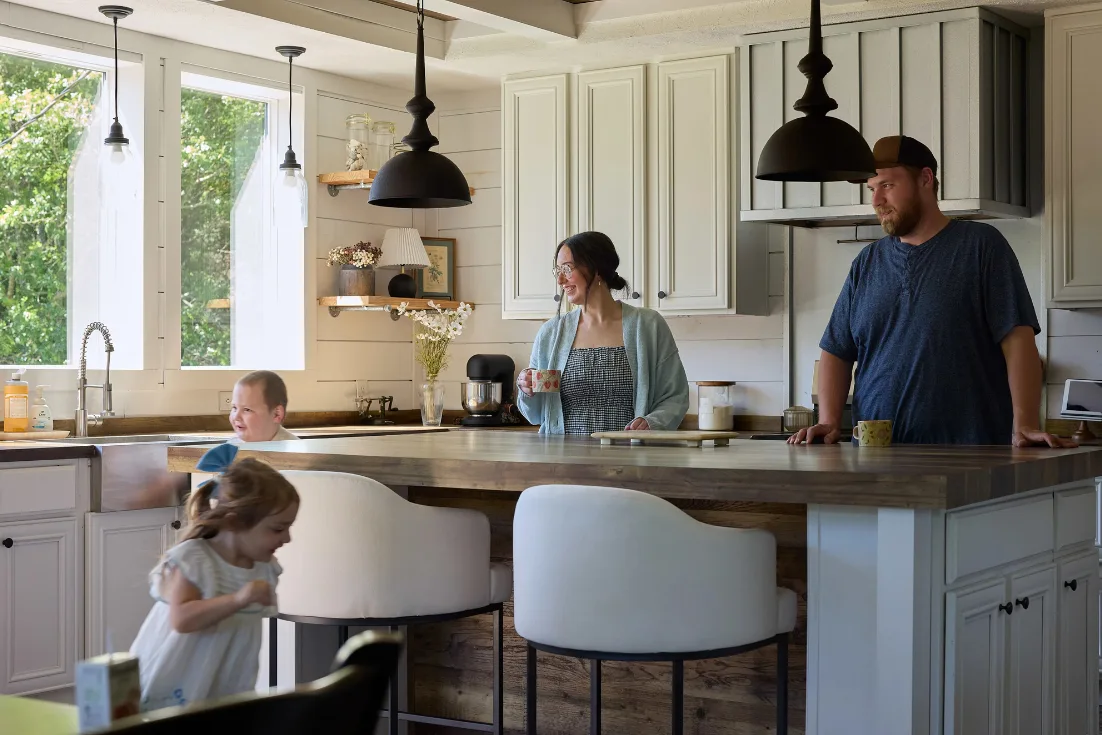 The Isaacks family in their country Lulamae kitchen with Courtney and Ethan standing at the butcher block kitchen island watching their two young children run around it.