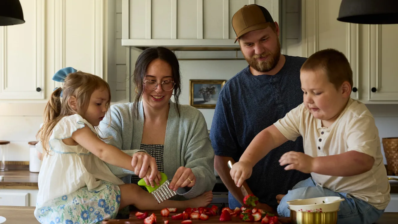The Isaacks family cuts strawberries together in the kitchen.