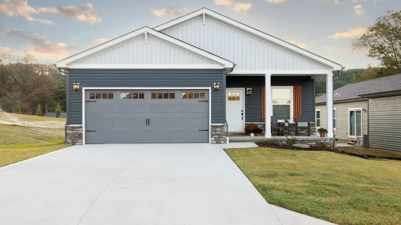 The exterior of a new construction home with blue siding, a gray garage door, a front porch with white columns, and a white front door.