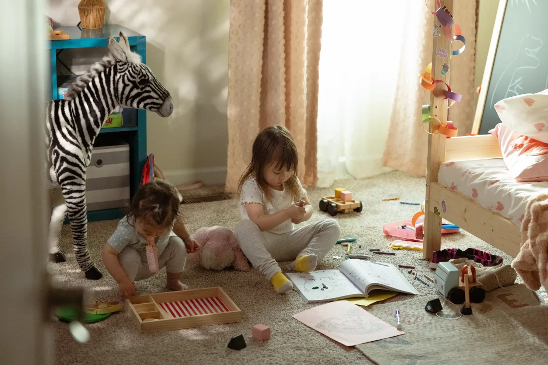 Two little girls play in their bedroom surrounded by toys and coloring books.