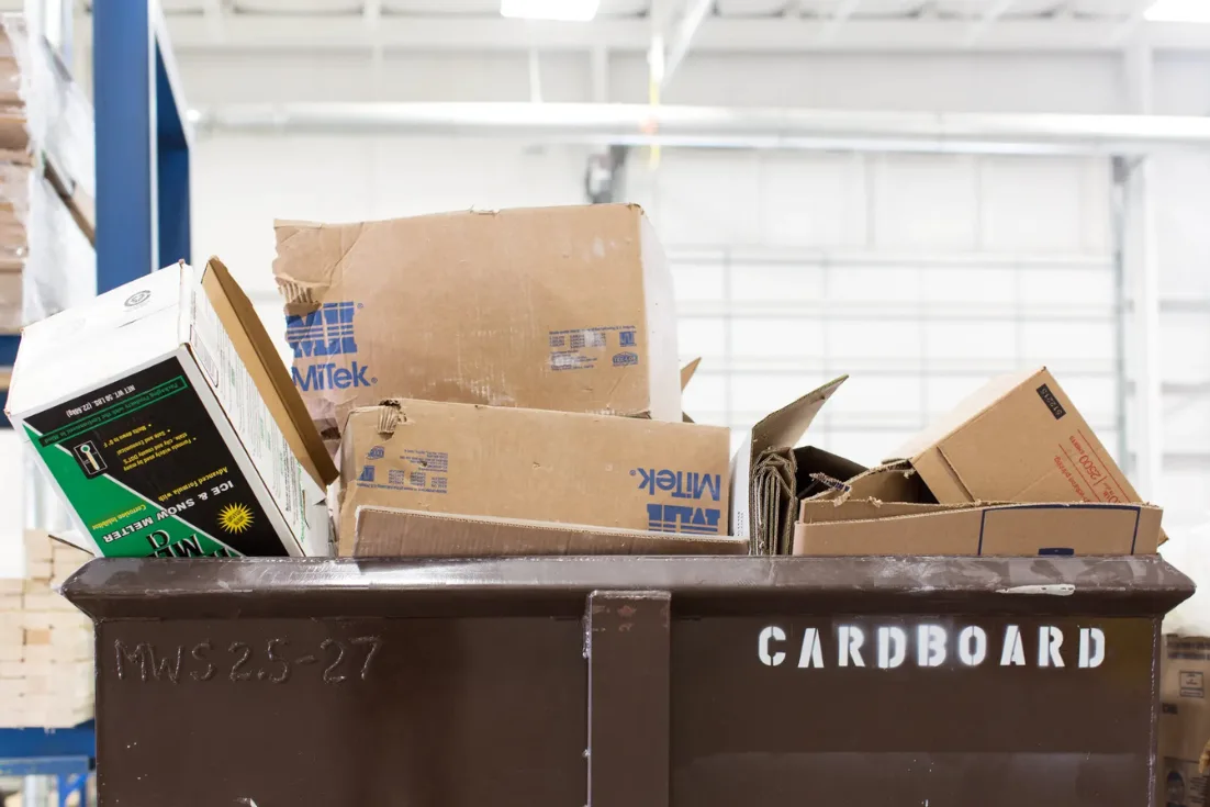 Empty carboard boxes sit in a large metal recycling bin in a Clayton home building facility.