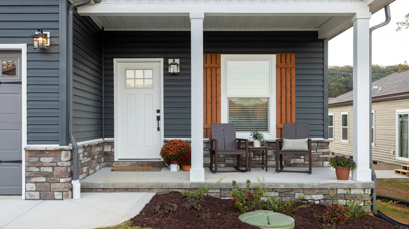 A close-up of a blue home's front porch decorated with metal chairs and potted plants.