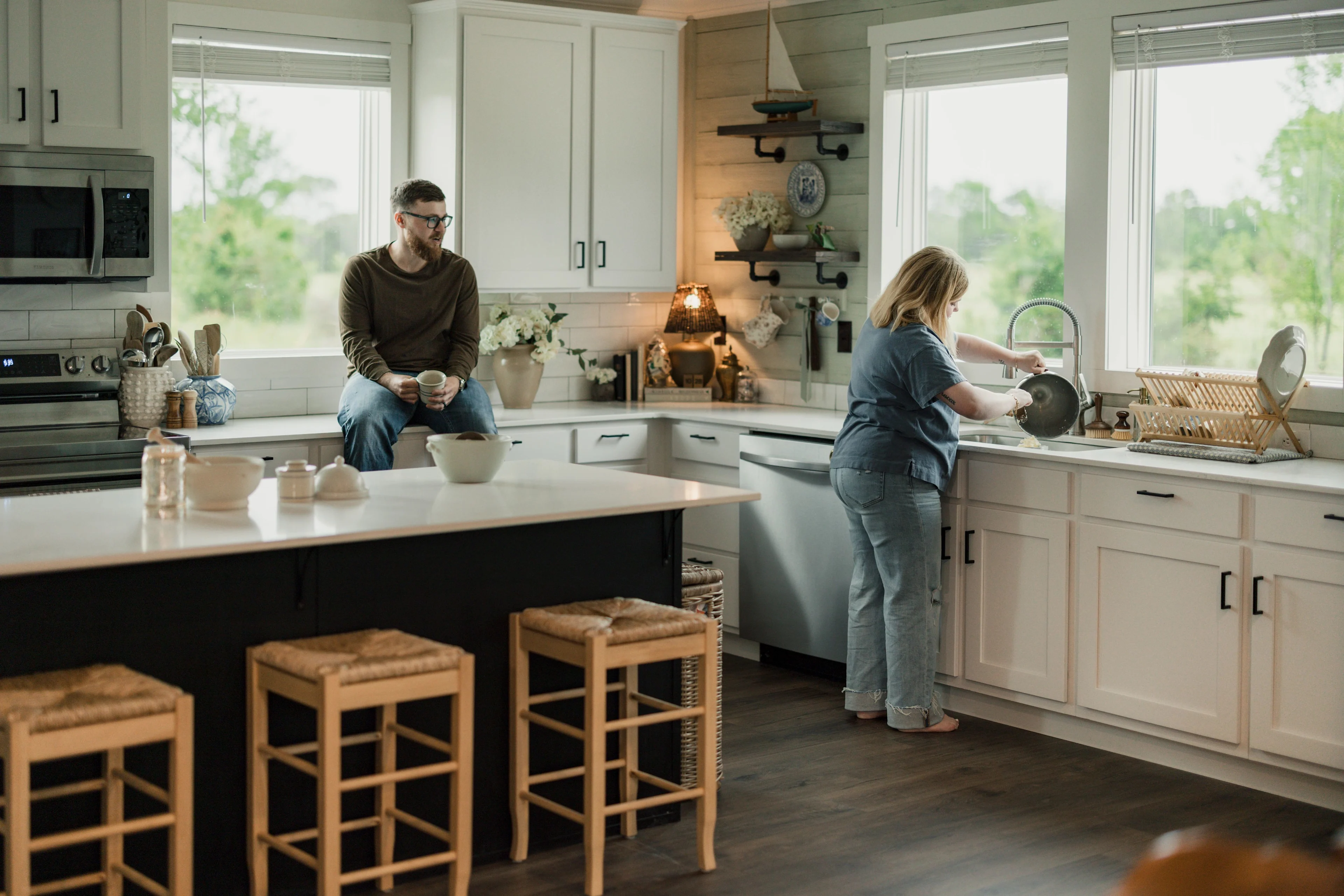 Koven washing dishes at her kitchen sink and Josh sits on the countertop drinking coffee.