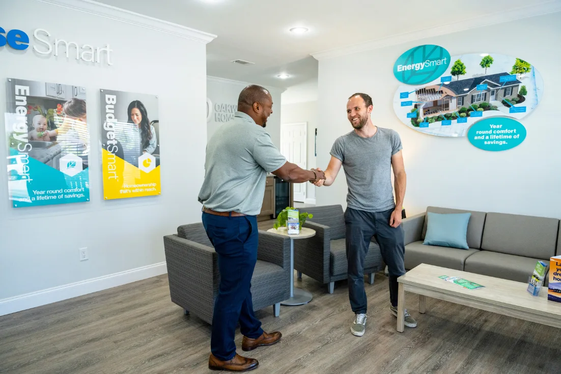 A home consultant shakes hands with a visiting customer in a blue waiting area.