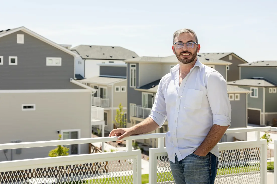 Justin Jones smiles while leaning on his balcony, the new construction site-built homes of his neighborhood seen behind him on a sunny day.