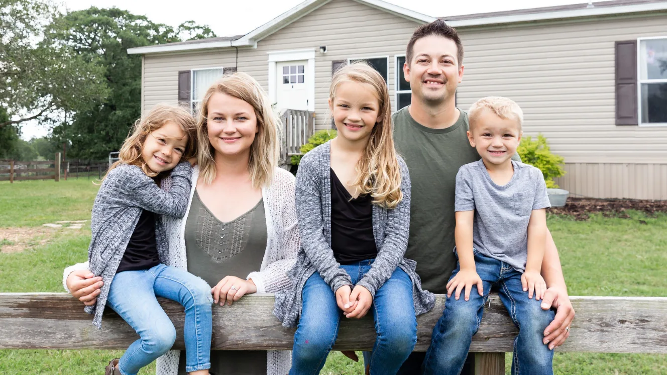 Family sits on couch in farmhouse living room in front of a shiplap wall.