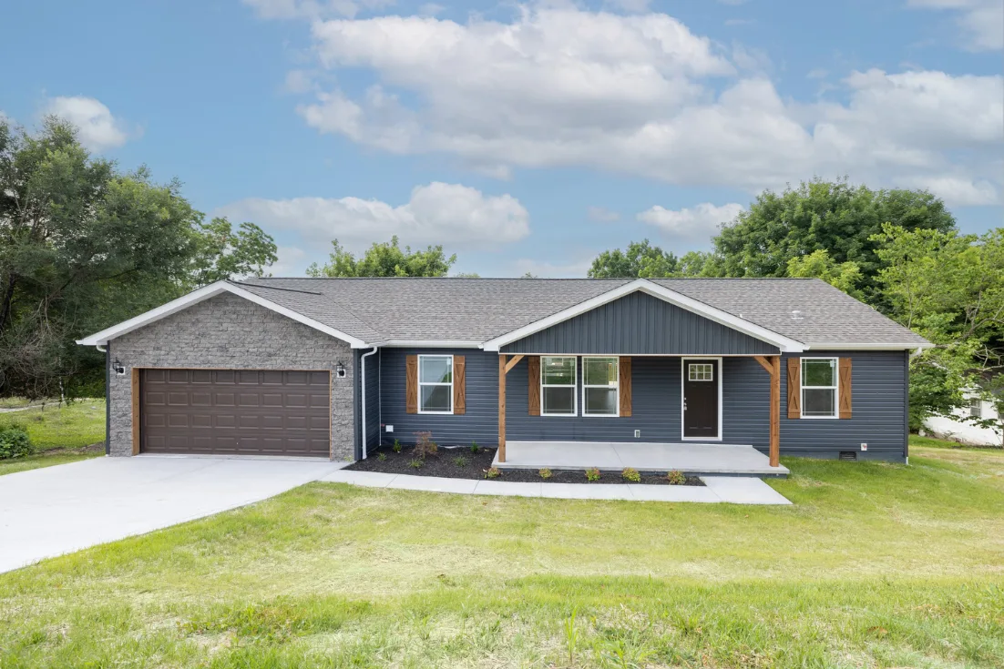 An exterior of a CrossMod home with a open front porch, blue siding, and an attached garage under a blue sky full of fluffy clouds.