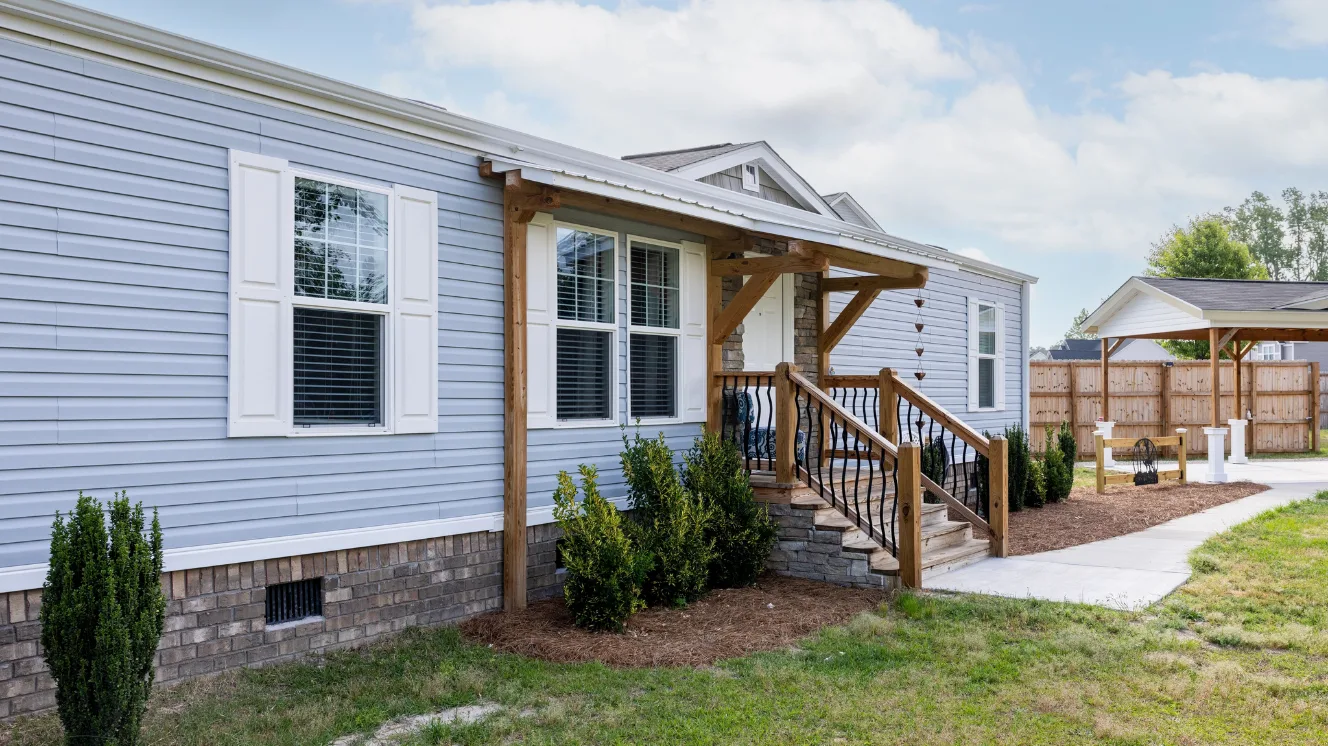An exterior of a modern manufactured home with blue siding, white shutters, and brick stairs.