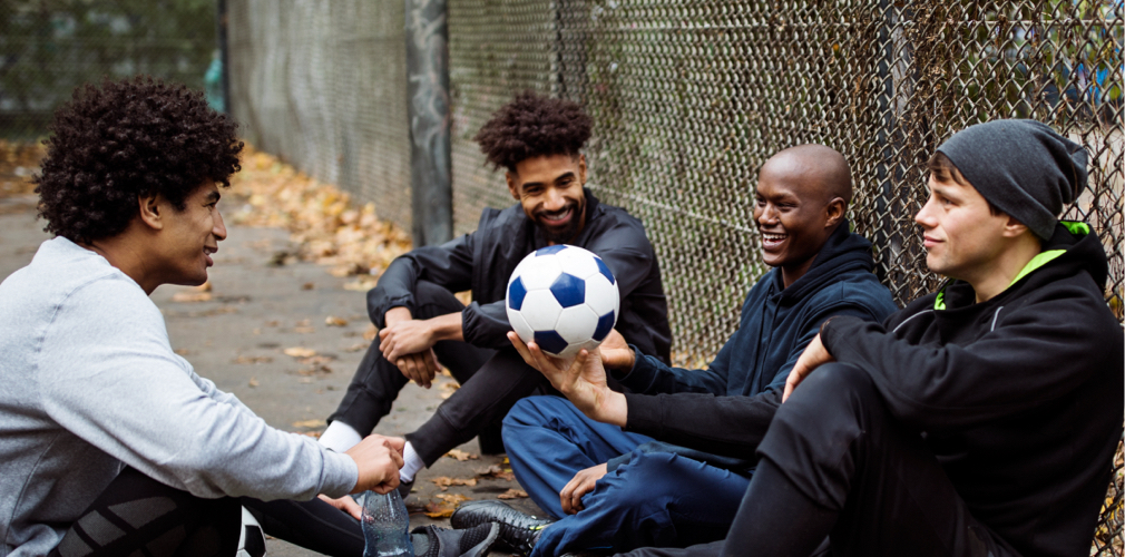 4 men sitting in a park with a soccer ball.