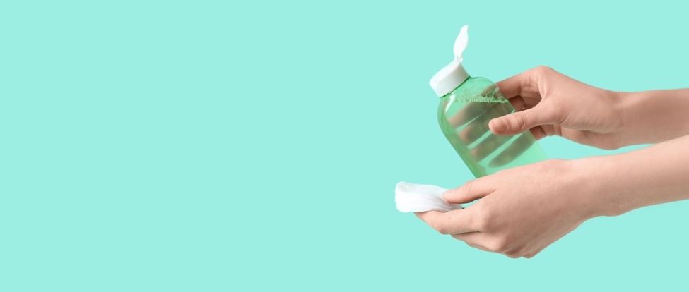 Hands holding bottle of micellar water and cotton pads on turquoise background with space for text.