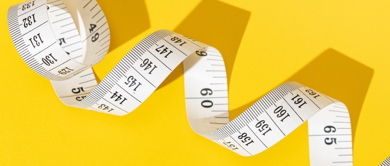 Measuring tape unravelling against yellow background.