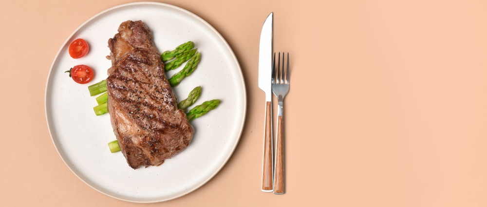 Grilled ribeye steak with asparagus and cherry tomatoes on white plate on beige background  top view healthy food copy space 