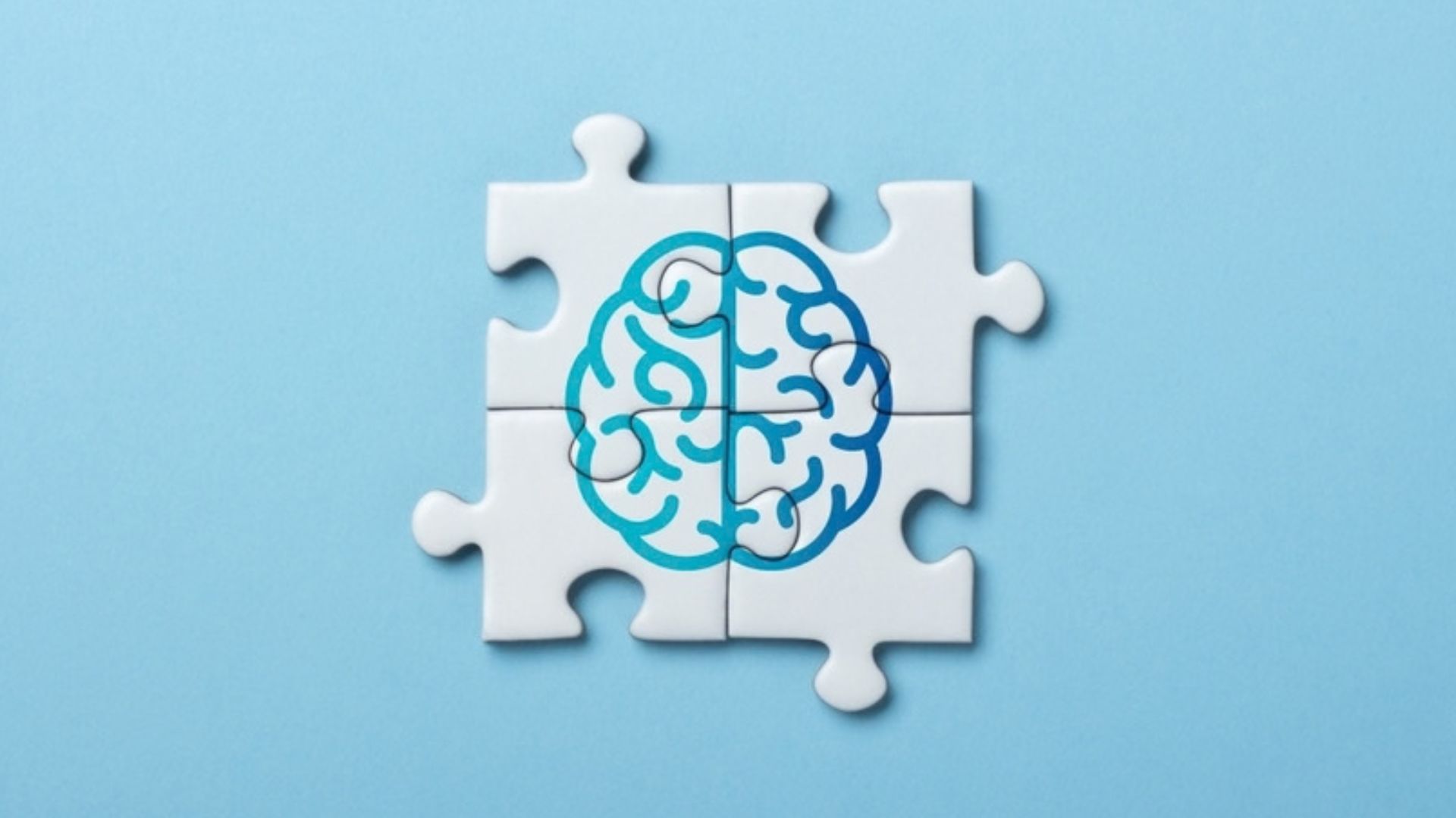 Blue line drawing of brain on four connected jigsaw pieces against a blue background.