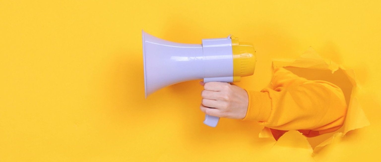 Arm bursting out of bright yellow background holding yellow and white megaphone.