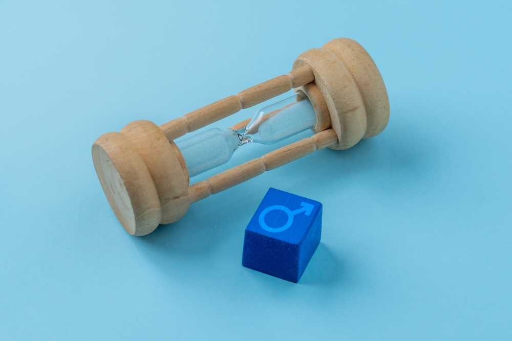 A wooden hourglass and a blue cube with the male symbol. Male health, andropause, ageing concept.