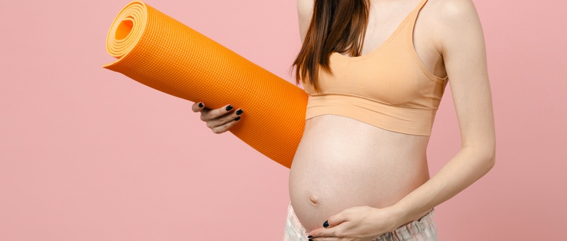 Young strong sporty fitness pregnant woman keeping hands on big belly stomach tummy with baby holding yoga mat isolated on pastel pink background studio. Maternity family pregnancy expectation concept