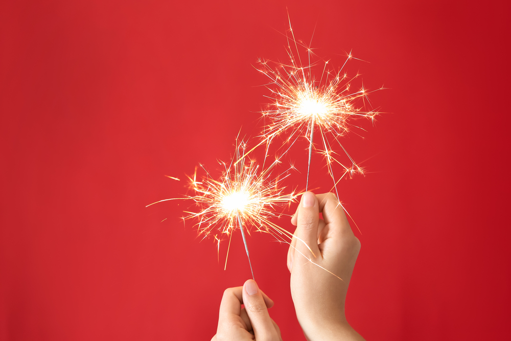 Female hands holding bright burning sparklers on red background.
