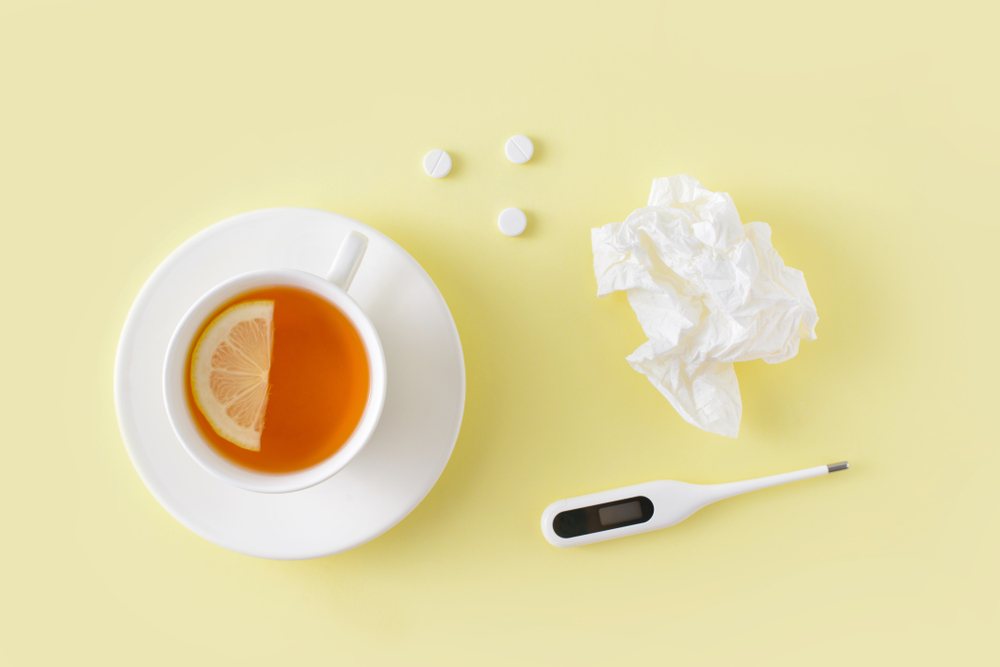Pills, napkins for the nose, thermometer, and cup of tea on yellow background. Cold and flu treatment set.