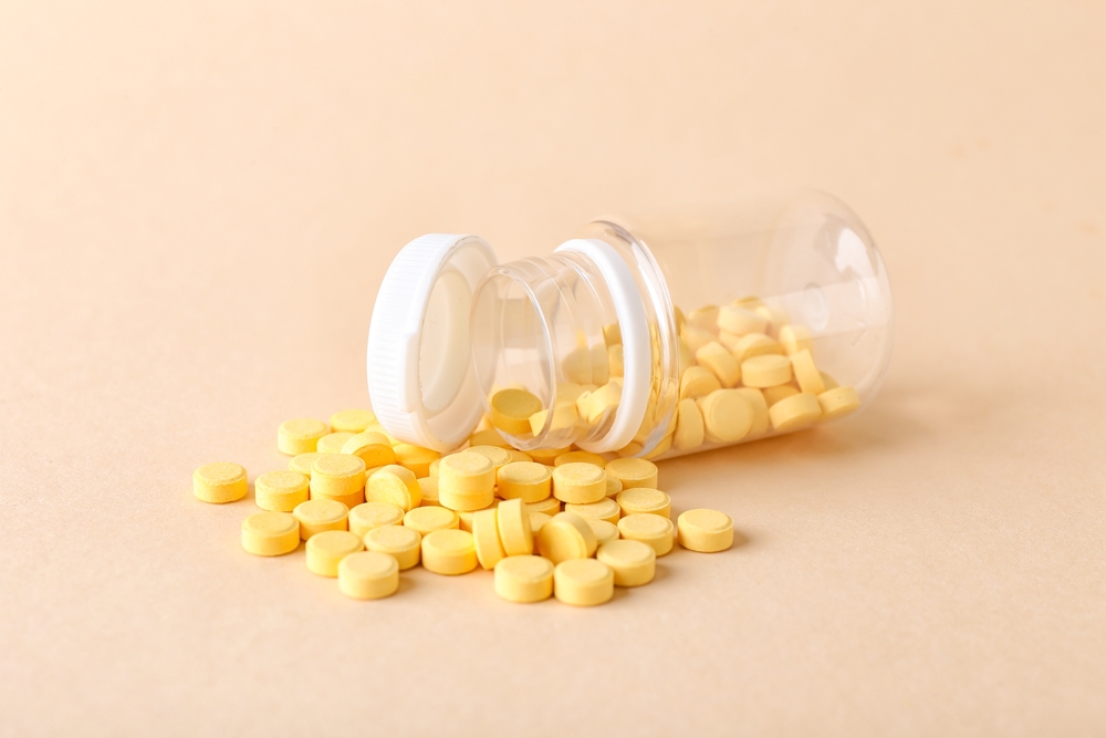 Overturned medicine bottle with scattered folic acid tablets against a pale pink background.
