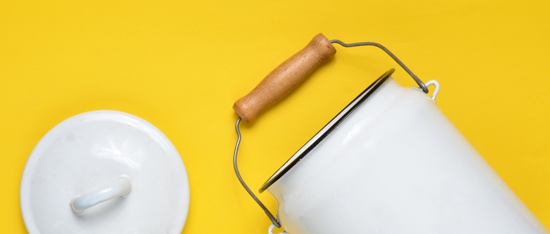 White enameled milk can on bright yellow background.
