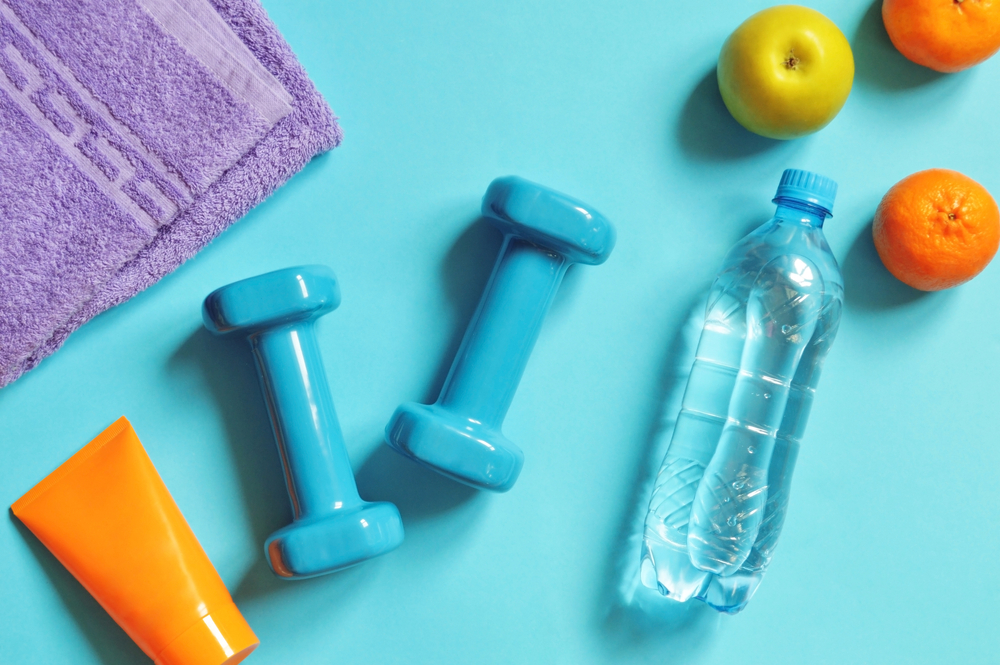 Excercise equipment with fruit, water, and body cream against blue background.