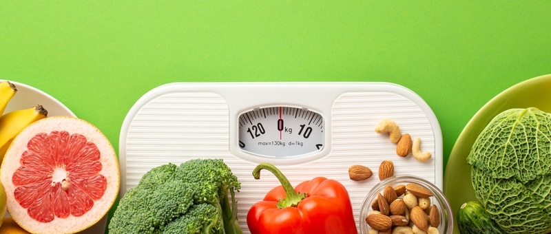 Top view photo of plates with fruits and vegetables grapefruit apple bananas cauliflower pepper cabbage cucumber nuts and scales on isolated green background.