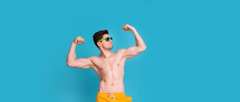 Full body photo of handsome young guy raises fists flexing posing dressed stylish yellow shorts isolated on blue colour background.