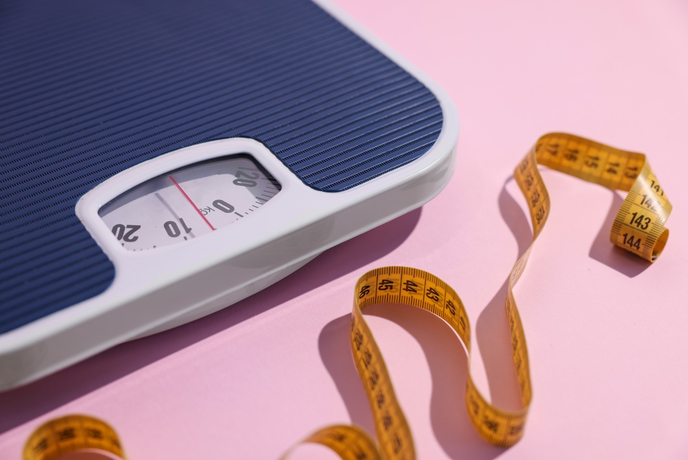 Blue and white weighing scales with yellow measuring tape against pink background.