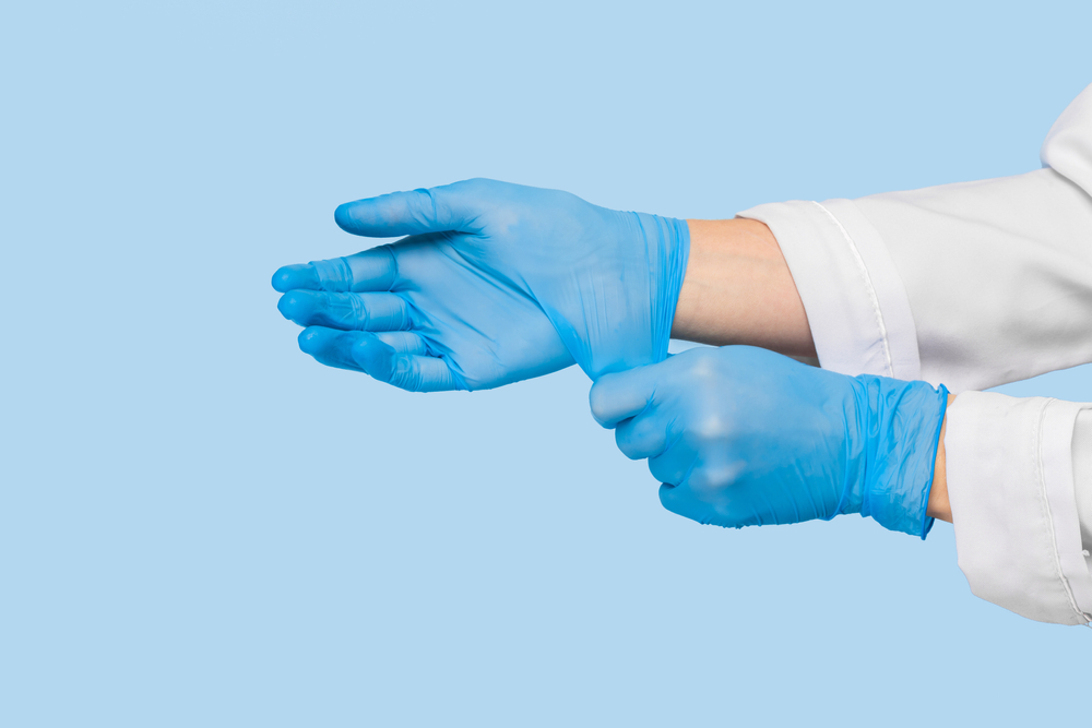 Blue surgical gloved hands against blue background.