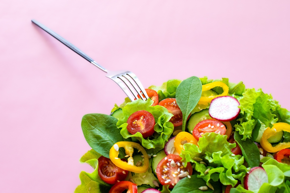 Bowl of colourful salad with fork against pink background.