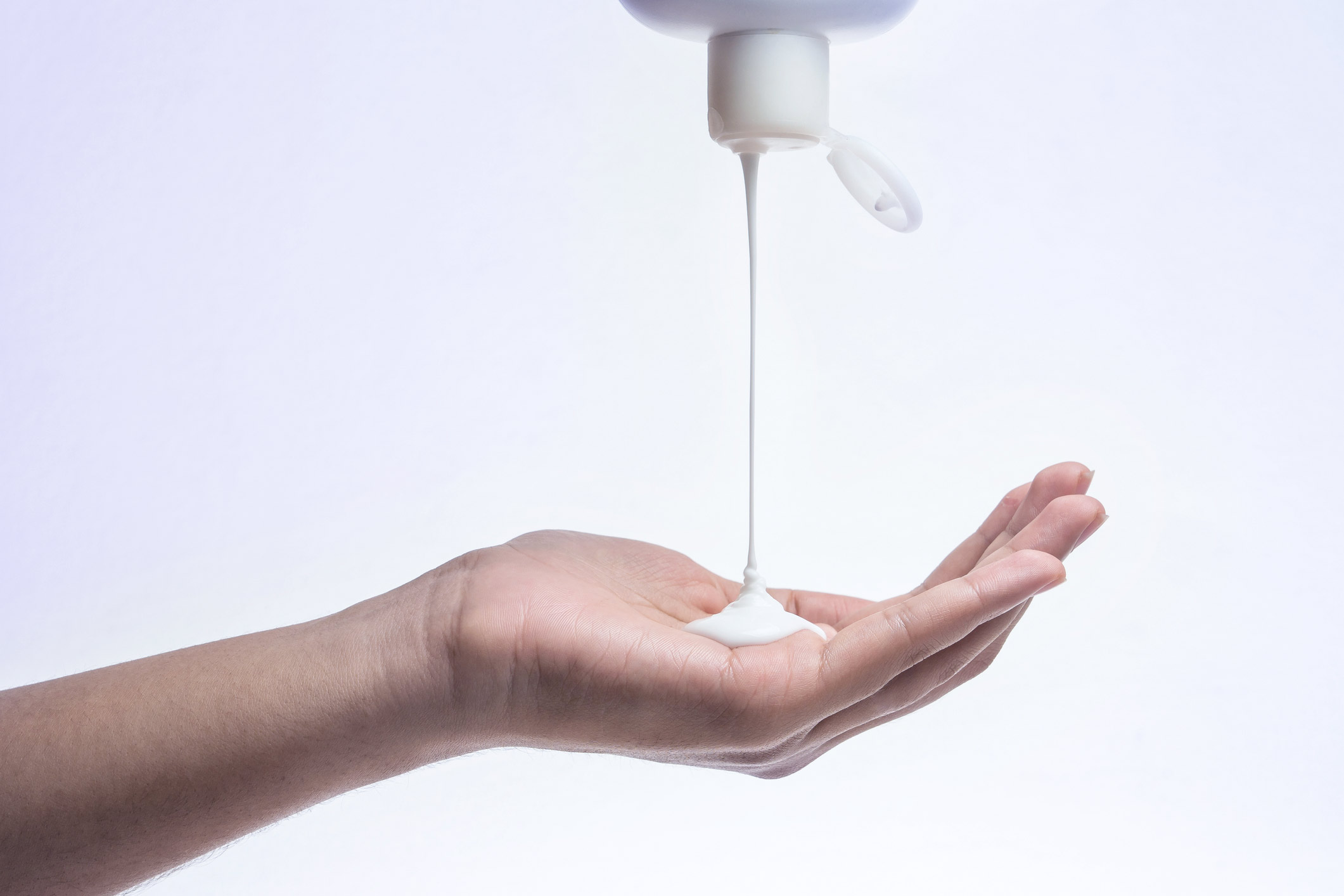 White liquid soap dispensing from a pump bottle onto an outstretched palm against a light background.