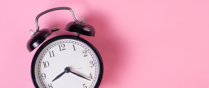 Black and white vintage analogue alarm clock against pink background.