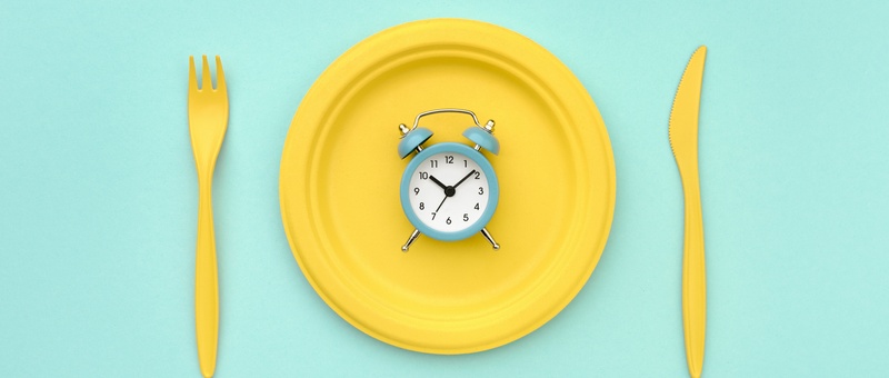 Alarm clock on yellow plate with cutlery against a blue background