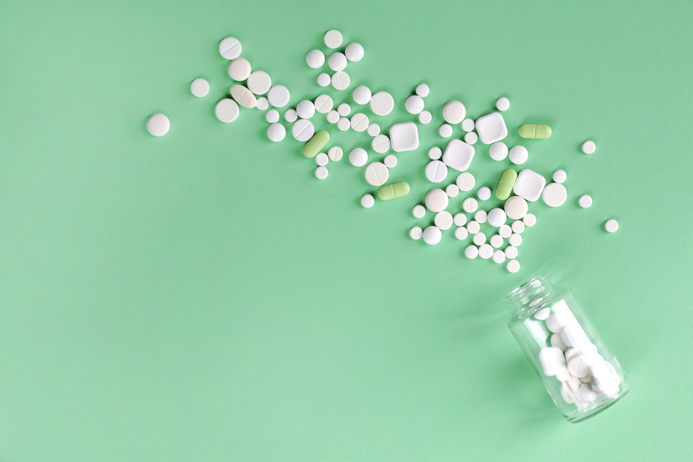 Overflowing medicine bottle with scattered pills against a green background.