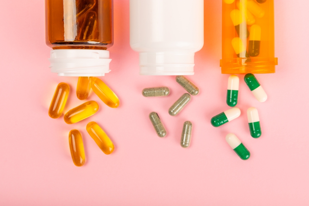 Three assorted pill bottles with medication and supplements spilling out against a pink background.