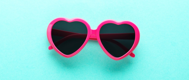 Pink heart shaped sunglasses on blue background.