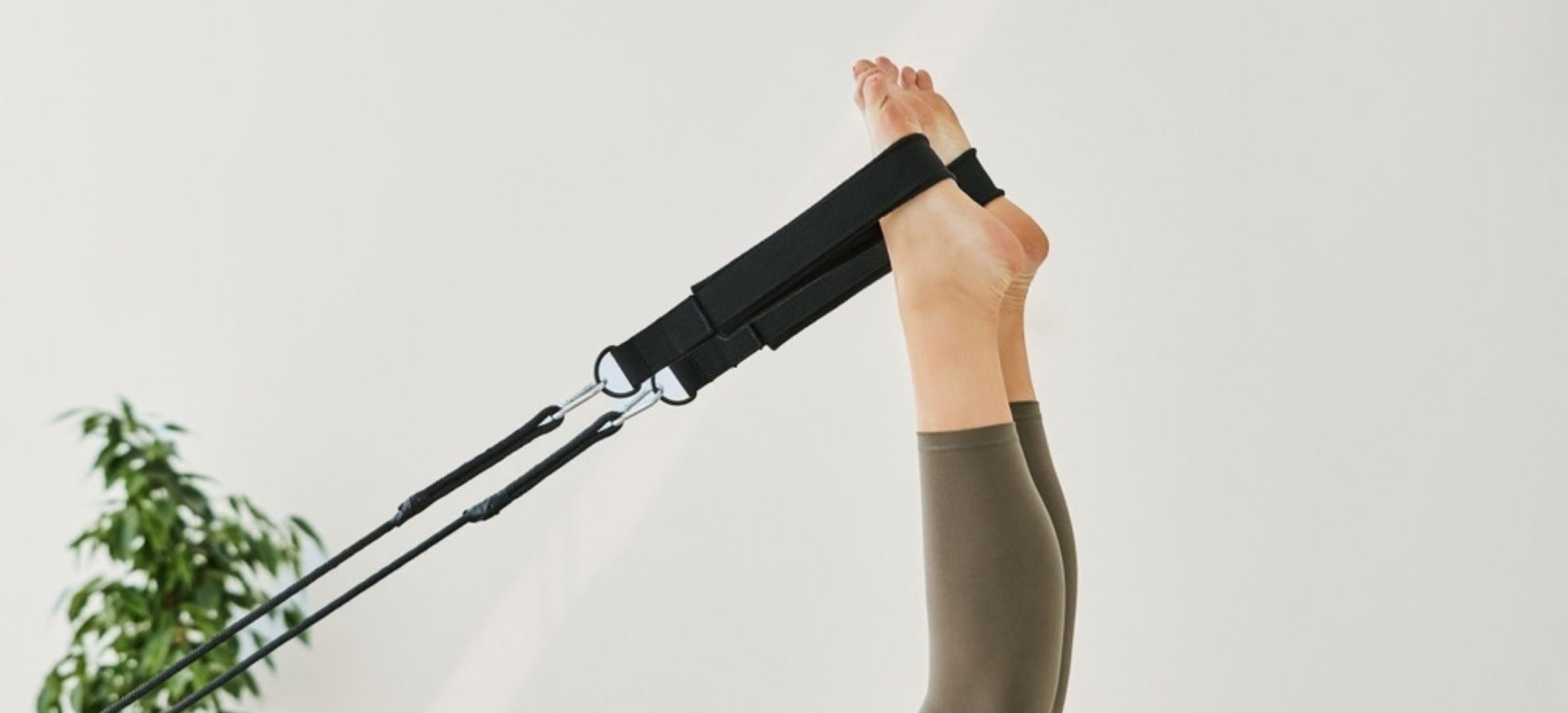 Close-up of feet on a Pilates reformer machine against bright background.