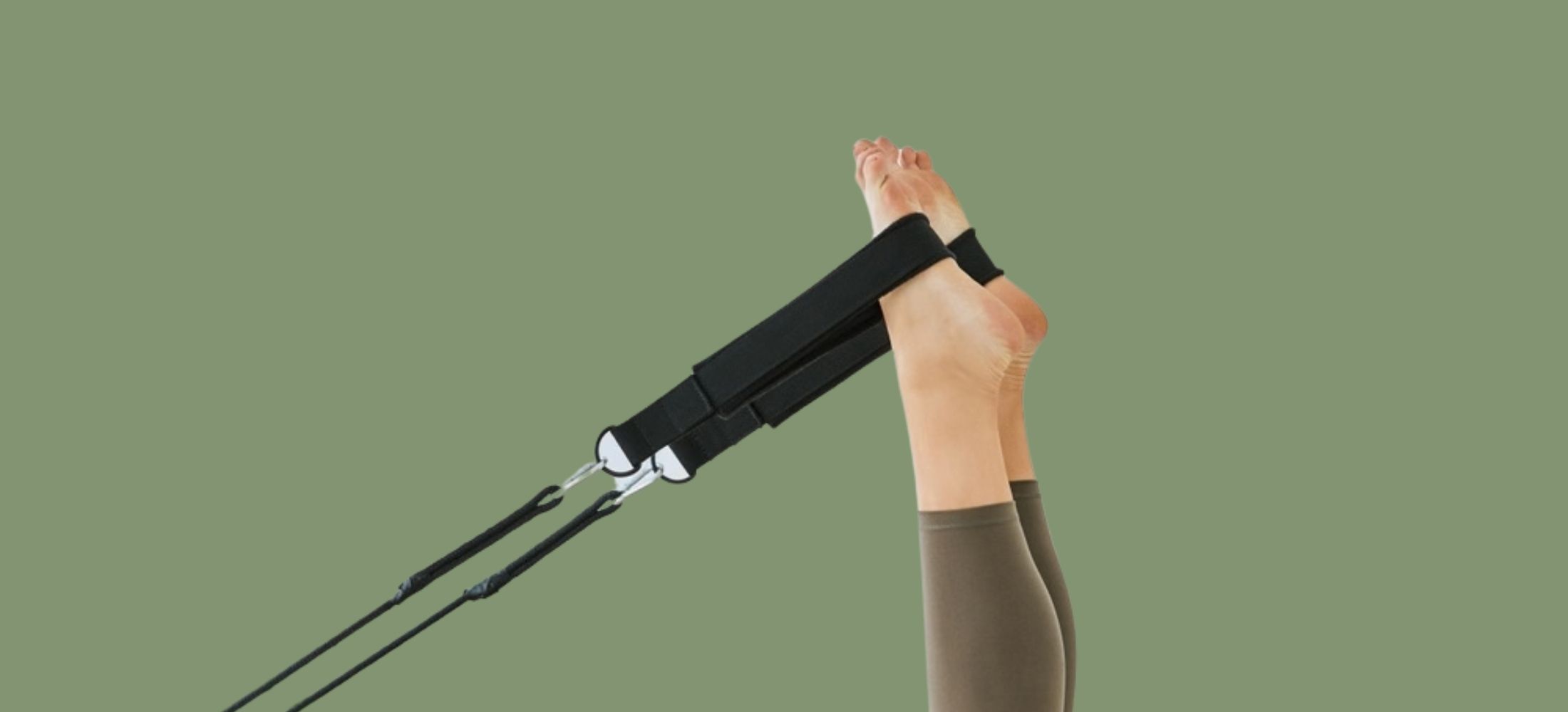 Close-up of feet on a Pilates reformer machine against green background.