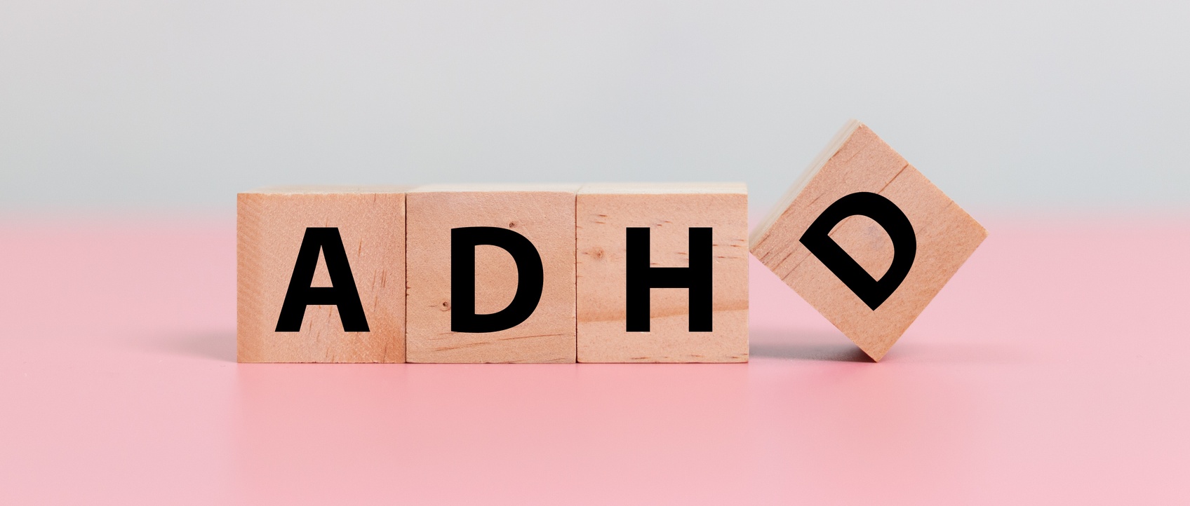 Wood cube block Abbreviation of ADHD on pink table. Attention Deficit Hyperactivity Disorder.