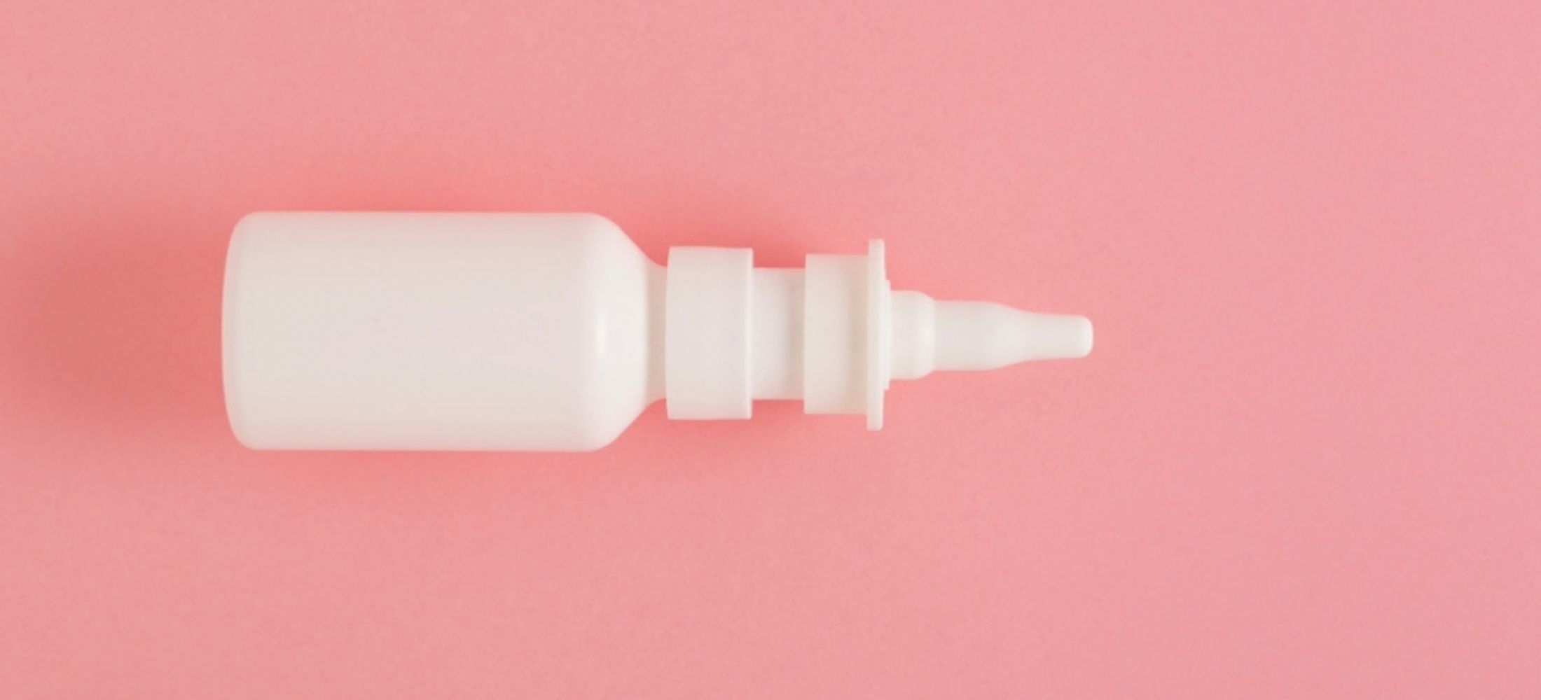 White nasal drops/nasal spray container against pink background.