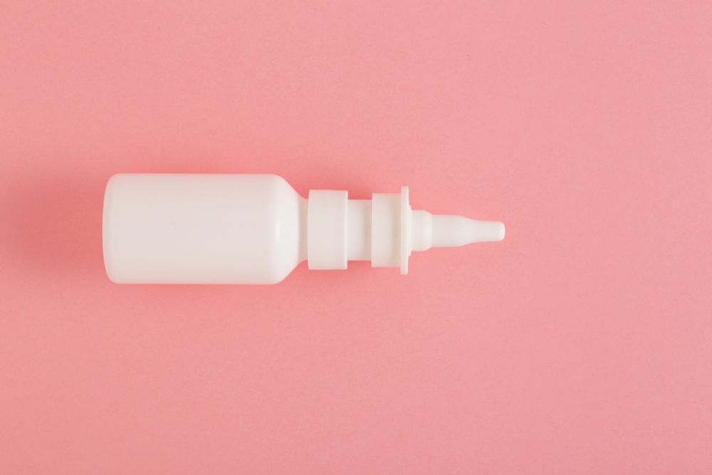 White nasal drops/nasal spray container against pink background.
