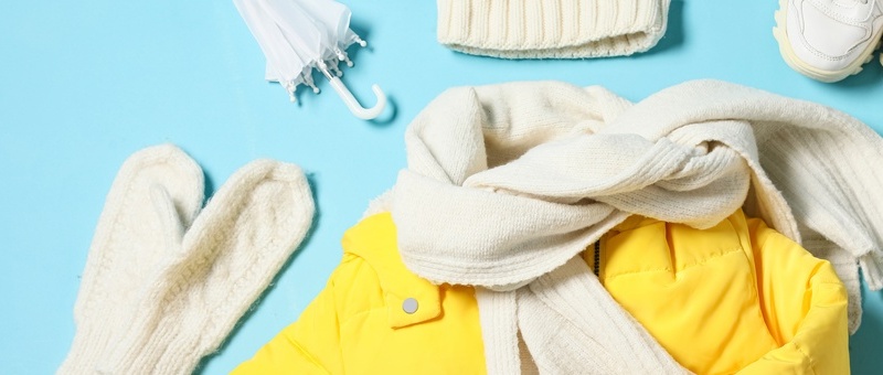 Children's yellow puffer jacket with scarf, gloves, sweater and mobile phone on blue background.